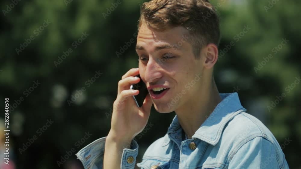 happy guy in denim jacket speaks over telephone standing against blurred trees on sunny day close view slow motion happy guy in denim jacket speaks over telephone standing against blurred trees on sunny day close view slow motion