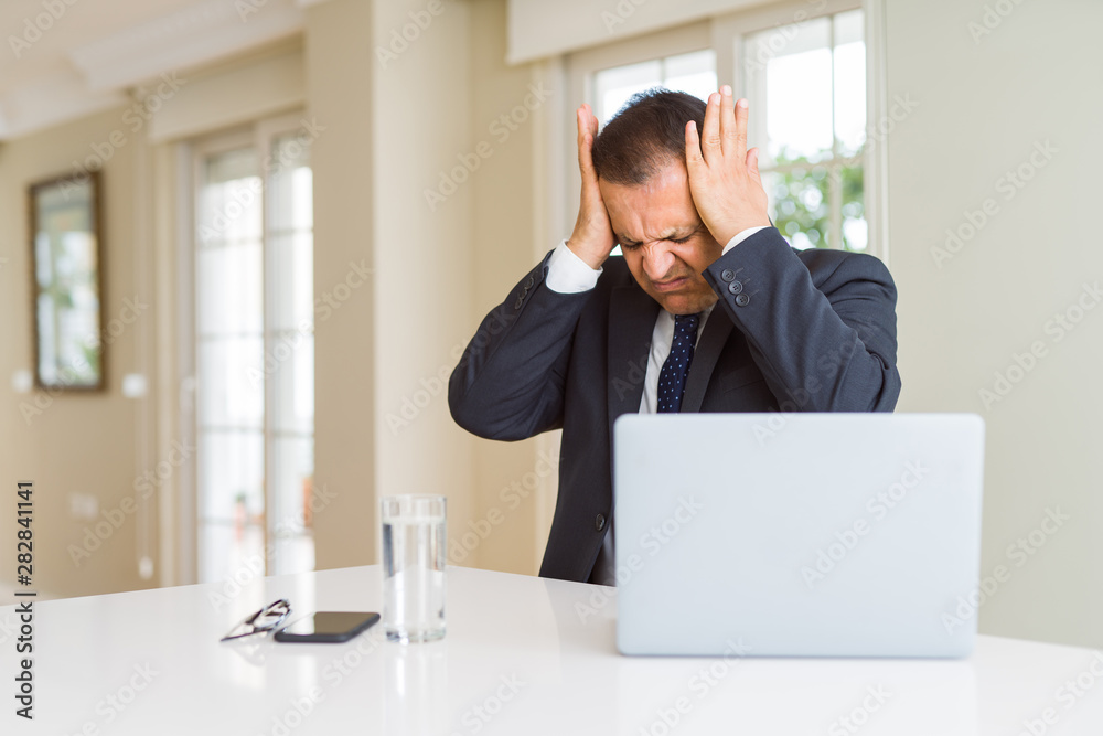 Middle age business man working with computer laptop suffering from headache desperate and stressed because pain and migraine. Hands on head.