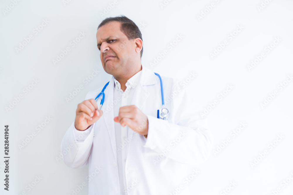 Middle age doctor man wearing stethoscope and medical coat over white background disgusted expression, displeased and fearful doing disgust face because aversion reaction. With hands raised. 