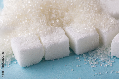 Heap of granulated sugar with cube on blue background. 