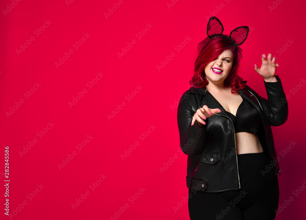 Cute sexy plus size brunette with black bunny ears in leather jacket and underwear posing on red background Cute sexy plus size brunette with black bunny ears in leather jacket and underwear posing on red background