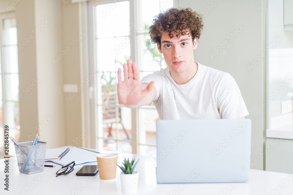 Young student man working and studying using computer laptop with open hand doing stop sign with serious and confident expression, defense gesture