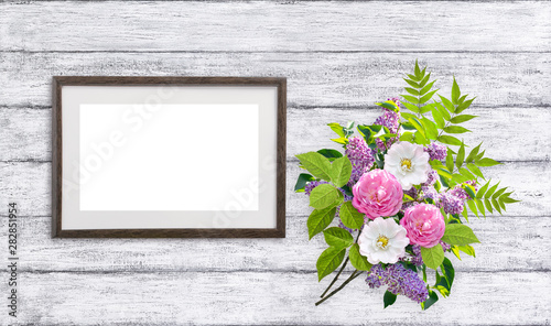 Floral bouquet with lilacs, magnolia and dog roses (briar) flowers and empty motivationall picture frame on shabby wooden planks background. Copy space for photo or text. photo