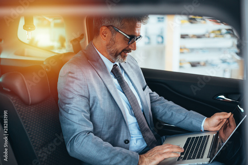 senior businessman using laptop sitting backseat of car © cherryandbees