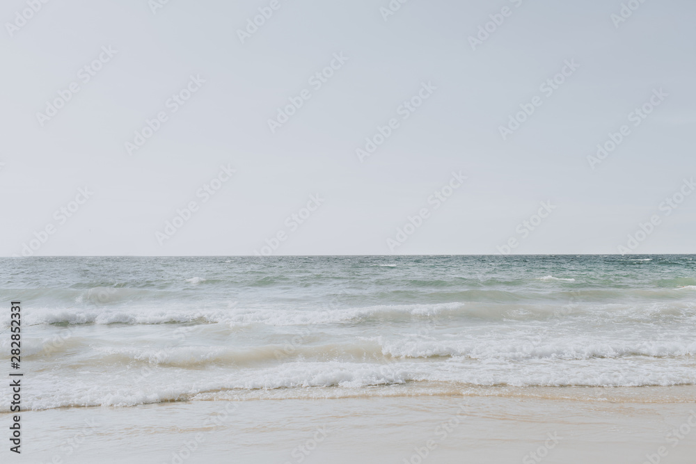 Beautiful tropical beach view with white sand and blue sea with waves on Phuket, Thailand. Minimal composition with neutral colors. Summer concept. Natural background.