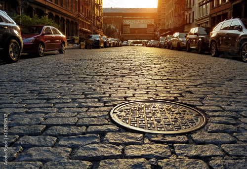 Sunlight shining on a cobblestone street and manhole cover in New York City photo