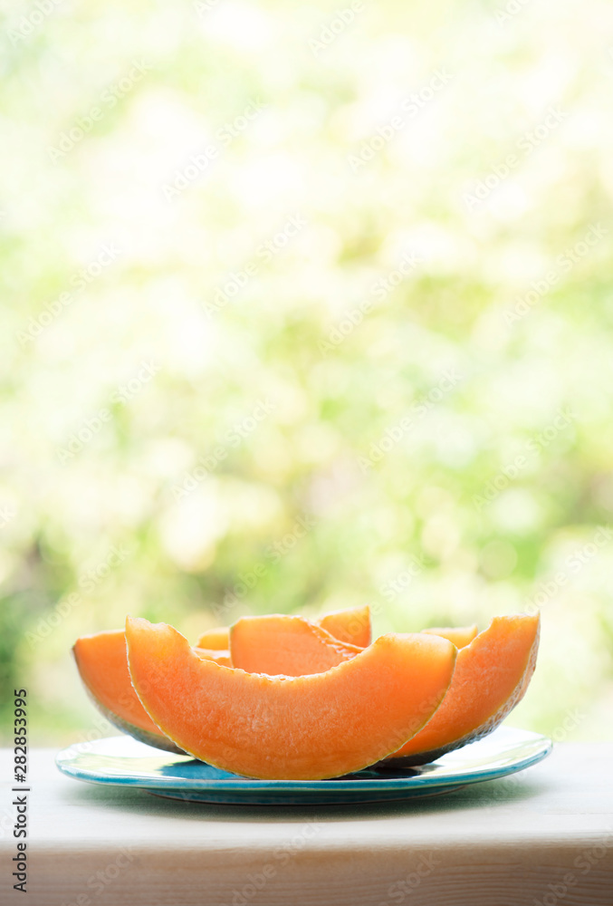 Pieces of juicy fresh cantaloupe melon on a wooden table against the background of the garden. Selective focus, bokeh, copy space. Bright summer sunny background with food. Pieces of juicy fresh cantaloupe melon on a wooden table against the background of the garden. Selective focus, bokeh, copy space. Bright summer sunny background with food.