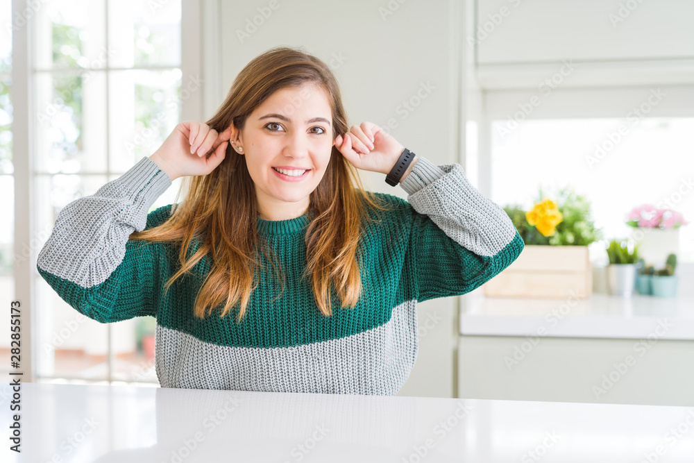Young beautiful plus size woman wearing casual striped sweater Smiling pulling ears with fingers, funny gesture. Audition problem