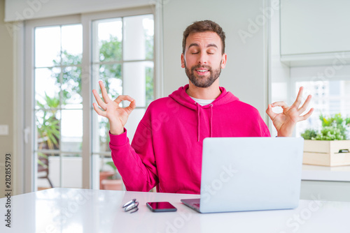 Handsome man working using computer laptop relax and smiling with eyes closed doing meditation gesture with fingers. Yoga concept.