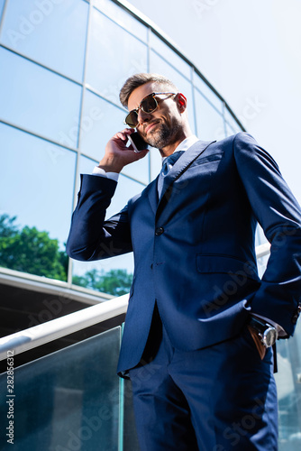 low angle view of handsome man in suit and glasses talking on smartphone