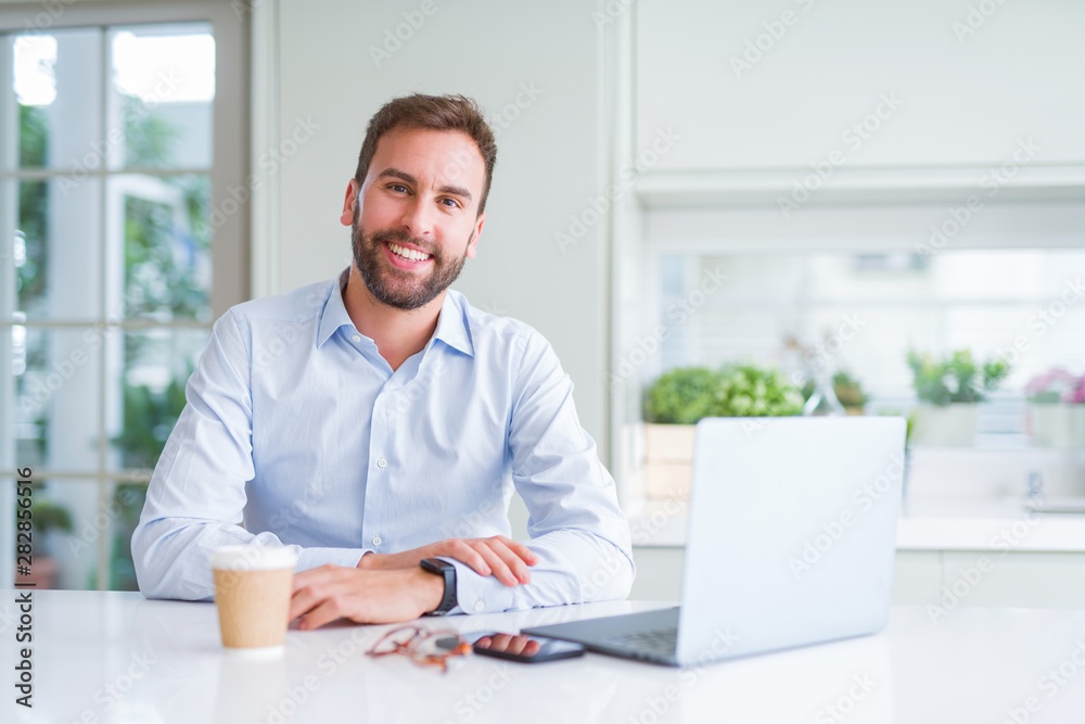 Handsome man working using computer laptop and drinking a cup of coffee with a happy face standing and smiling with a confident smile showing teeth