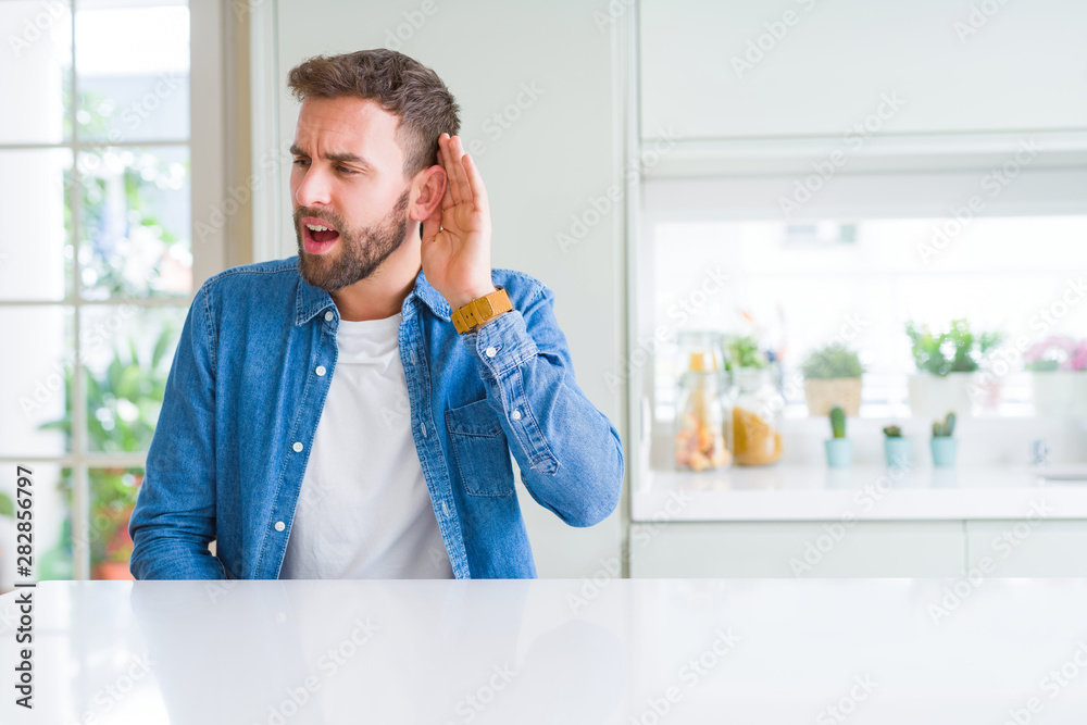 Handsome man at home smiling with hand over ear listening an hearing to rumor or gossip. Deafness concept. Handsome man at home smiling with hand over ear listening an hearing to rumor or gossip. Deafness concept.