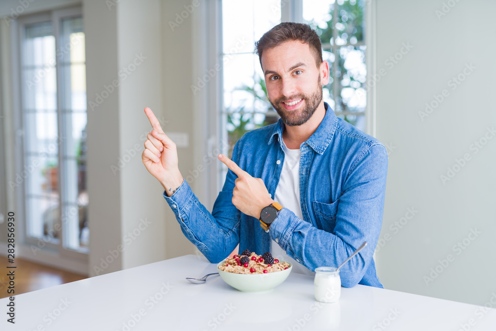 Handsome man eating cereals for breakfast at home smiling and looking at the camera pointing with two hands and fingers to the side. Handsome man eating cereals for breakfast at home smiling and looking at the camera pointing with two hands and fingers to the side.