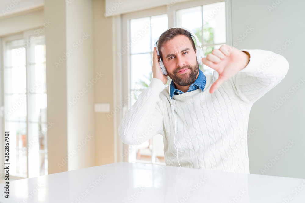 Handsome man wearing headphones and listening to music with angry face, negative sign showing dislike with thumbs down, rejection concept