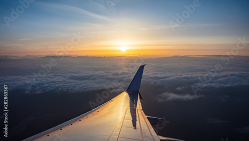 Sunrise view out of an airplane window. Plane flying over the clouds.