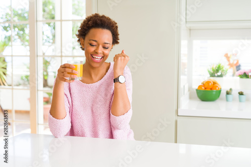 Young african american woman driking orange juice at home screaming proud and celebrating victory and success very excited, cheering emotion