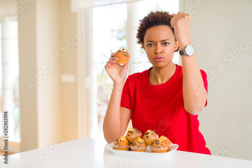 Young african american woman eating chocolate chips muffins annoyed and frustrated shouting with anger, crazy and yelling with raised hand, anger concept