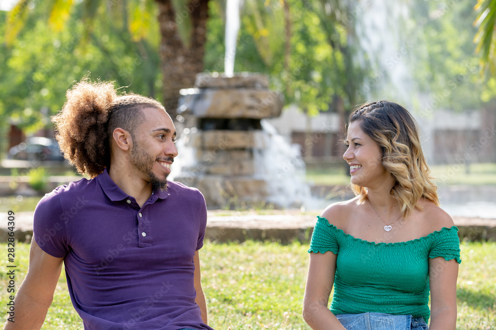 happy young couple in love looking at each other smiling sitting in front of a fountain on the park lawn happy young couple in love looking at each other smiling sitting in front of a fountain on the park lawn