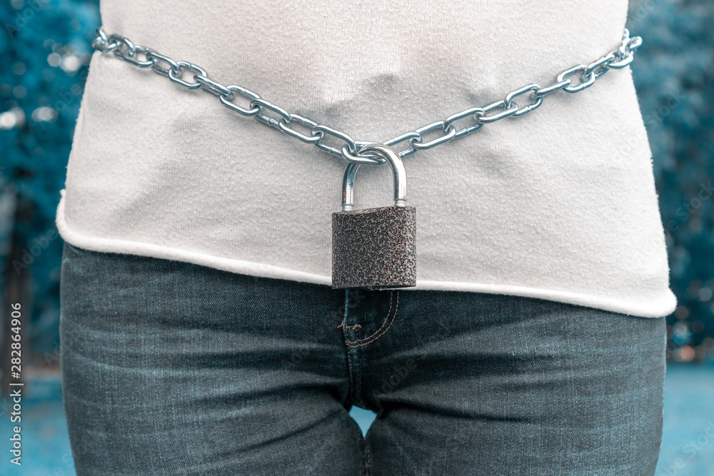 A metal chain with a lock on the lower back of a woman. The female is locked in its middle part in the chain and lock of the castle. The concept of sexual harassment and violence against a woman A metal chain with a lock on the lower back of a woman. The female is locked in its middle part in the chain and lock of the castle. The concept of sexual harassment and violence against a woman