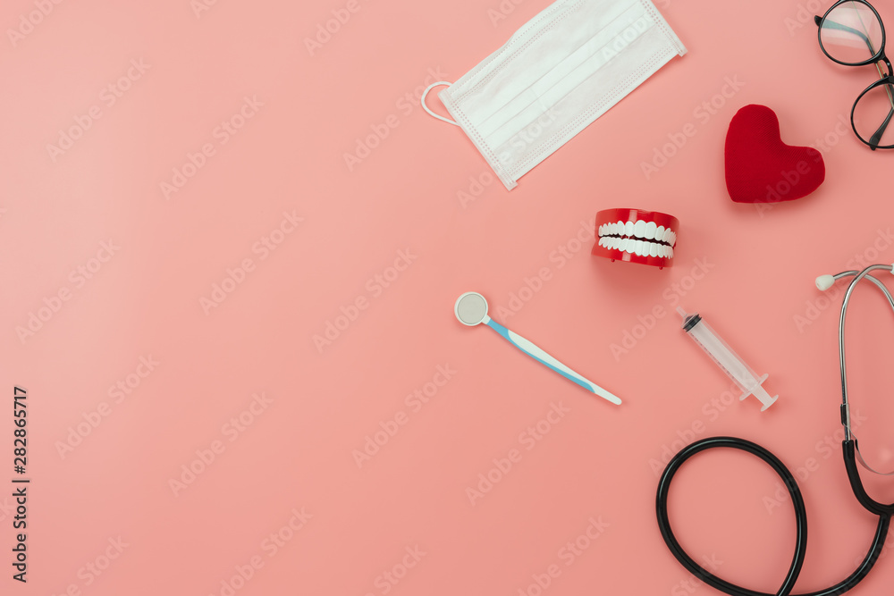 Table top view aerial image of accessories healthcare & medical background.Red heart & denture with essential objects on pink paper.Flat lay of idea for dentist doctor treat patient in hospital.