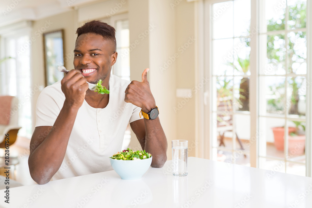 African american man eating fresh healthy salad happy with big smile doing ok sign, thumb up with fingers, excellent sign African american man eating fresh healthy salad happy with big smile doing ok sign, thumb up with fingers, excellent sign