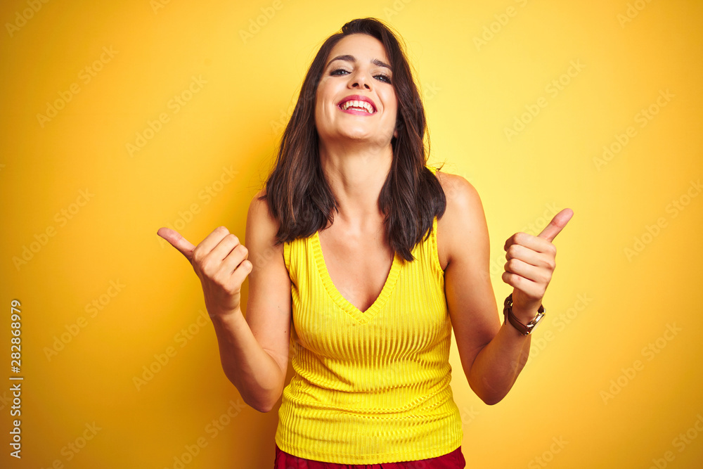 Young beautiful woman wearing t-shirt standing over yellow isolated background success sign doing positive gesture with hand, thumbs up smiling and happy. Cheerful expression and winner gesture. Young beautiful woman wearing t-shirt standing over yellow isolated background success sign doing positive gesture with hand, thumbs up smiling and happy. Cheerful expression and winner gesture.