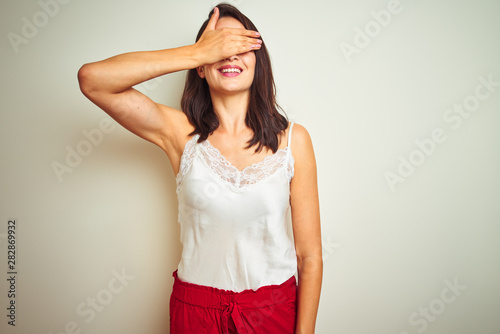 Young beautiful woman wearing t-shirt standing over white isolated background smiling and laughing with hand on face covering eyes for surprise. Blind concept.