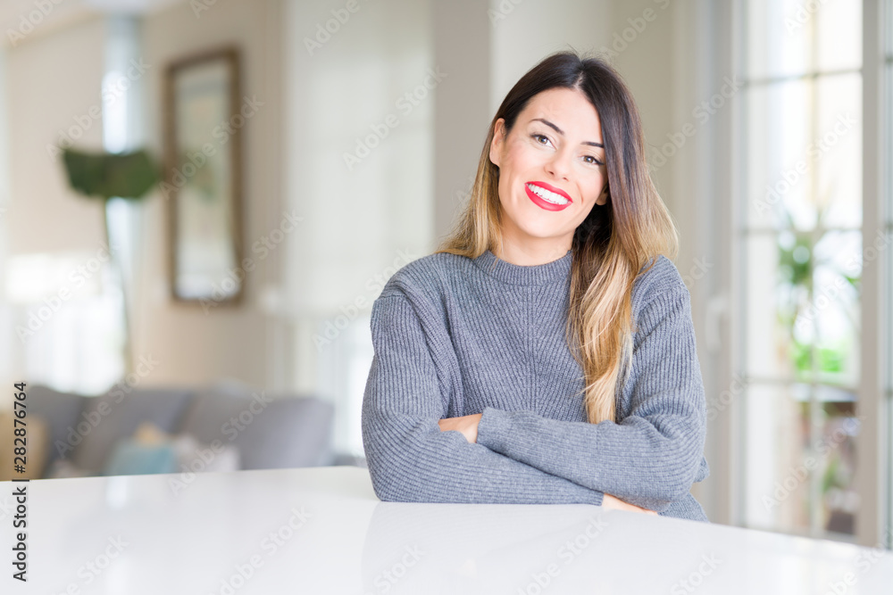 Young beautiful woman wearing winter sweater at home happy face smiling with crossed arms looking at the camera. Positive person. Young beautiful woman wearing winter sweater at home happy face smiling with crossed arms looking at the camera. Positive person.