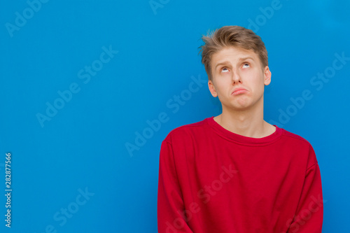 Closeup portrait of a sad guy standing on a blue background and looking up. 