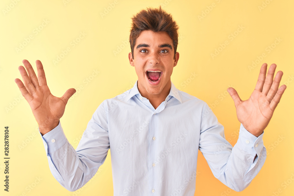 Young handsome businessman wearing elegant shirt over isolated yellow background celebrating crazy and amazed for success with arms raised and open eyes screaming excited. Winner concept Young handsome businessman wearing elegant shirt over isolated yellow background celebrating crazy and amazed for success with arms raised and open eyes screaming excited. Winner concept