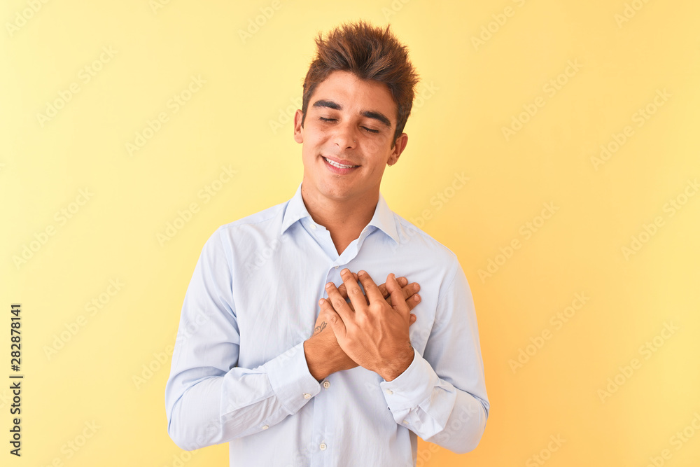 Young handsome businessman wearing elegant shirt over isolated yellow background smiling with hands on chest with closed eyes and grateful gesture on face. Health concept. Young handsome businessman wearing elegant shirt over isolated yellow background smiling with hands on chest with closed eyes and grateful gesture on face. Health concept.
