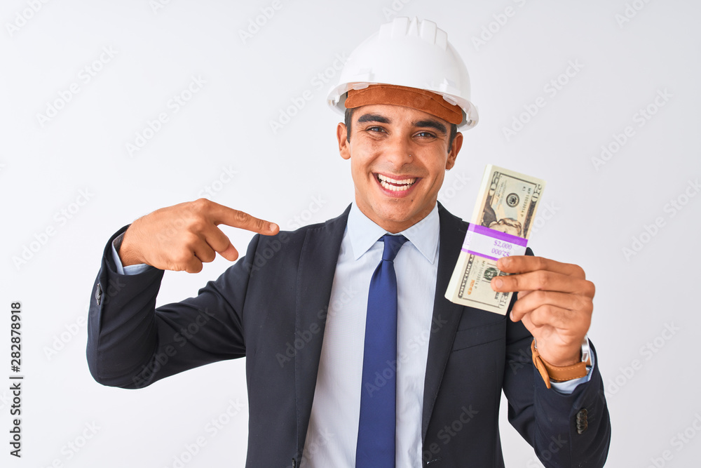 Young handsome architect man wearing helmet holding dollars over isolated white background with surprise face pointing finger to himself Young handsome architect man wearing helmet holding dollars over isolated white background with surprise face pointing finger to himself