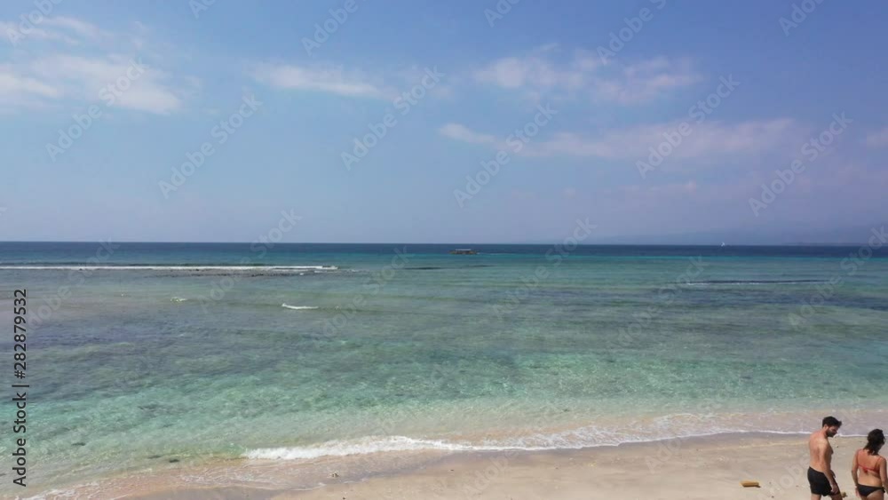erial view from drone of tourist couple walking on sandy beach in Gili Air Island Indonesia.Gili Islands are very popular tourist destinations for honeymooners. erial view from drone of tourist couple walking on sandy beach in Gili Air Island Indonesia.Gili Islands are very popular tourist destinations for honeymooners.