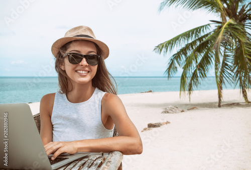 Young woman working with laptop computer on tropical island beach under palm trees Freelance  concept