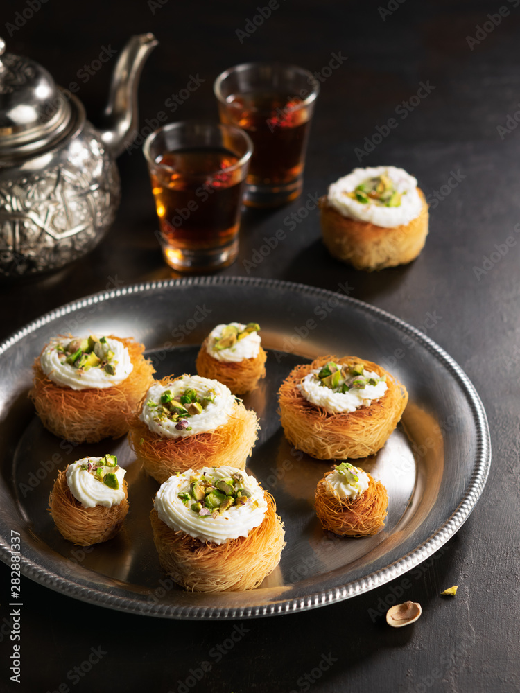 Kataifi, kadayif, kunafa, baklava pastry nest cookies with pistachios with tea. Cooking sweets turkish, or arabic traditional ramadan pastry dessert on a dark background.