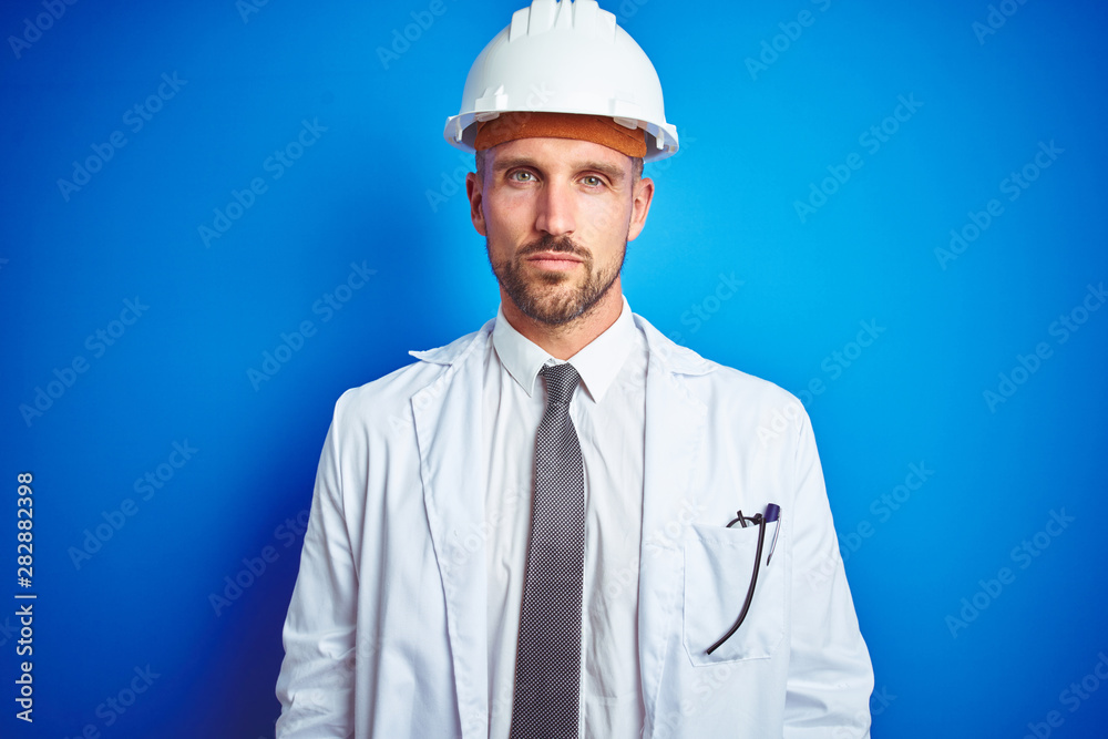 Young handsome engineer man wearing safety helmet over blue isolated background with serious expression on face. Simple and natural looking at the camera. Young handsome engineer man wearing safety helmet over blue isolated background with serious expression on face. Simple and natural looking at the camera.