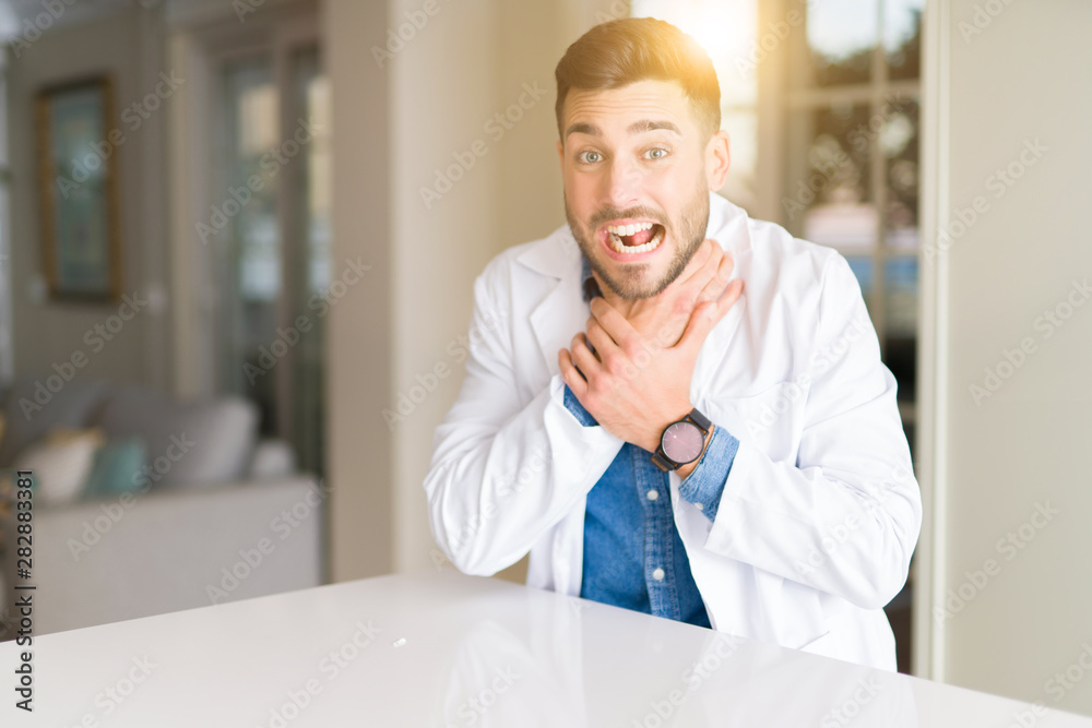 Fototapeta premium Young handsome doctor man at the clinic shouting and suffocate because painful strangle. Health problem. Asphyxiate and suicide concept.