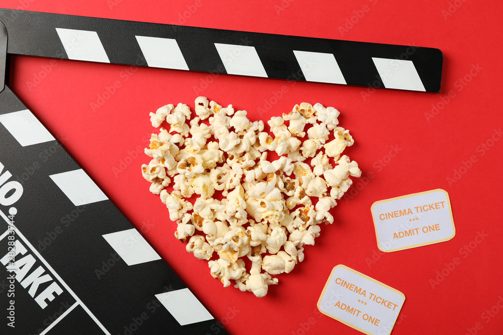 Heart laid out from popcorn, clapperboard and tickets on red background, top view