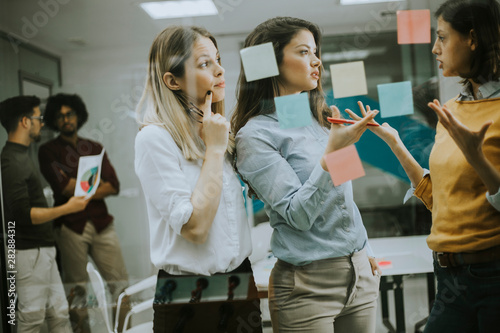 Young business women discussing in front of glass wall using post it notes and stickers