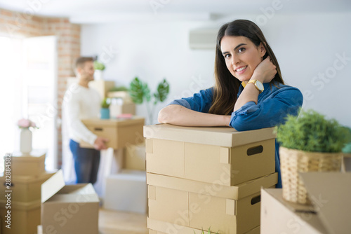 Young couple moving to a new home, beautiful woman smiling leaning on cardboard boxes