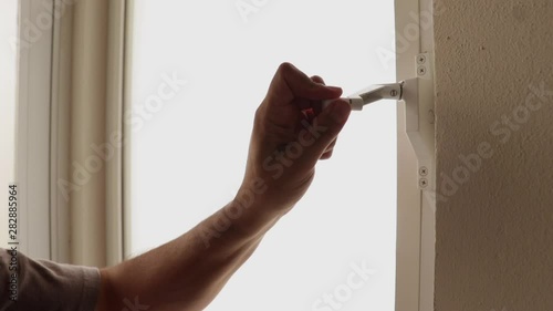 Detalle de una mano cerrando con una manija giratoria una ventana blanca traslúcida photo