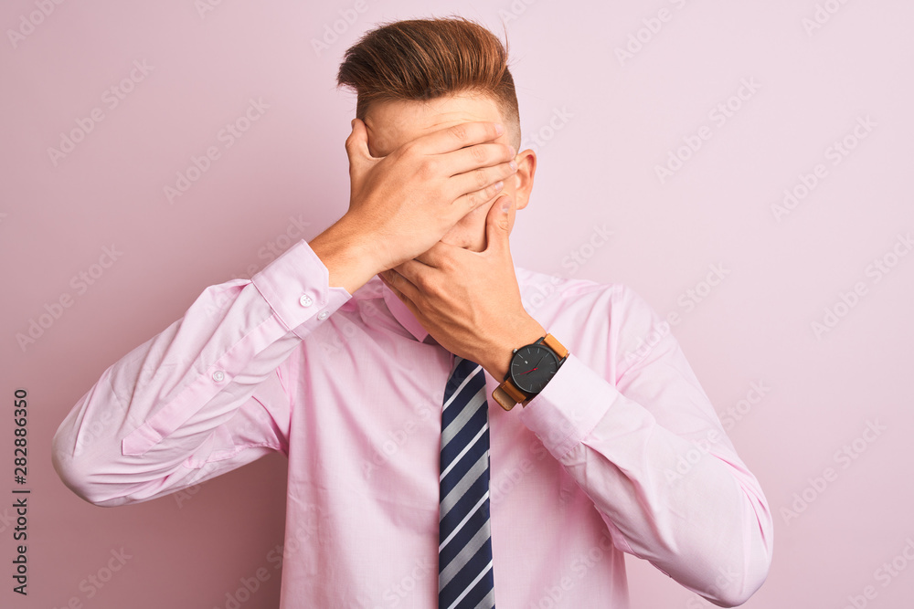 Young handsome businessman wearing shirt and tie standing over isolated pink background Covering eyes and mouth with hands, surprised and shocked. Hiding emotion Young handsome businessman wearing shirt and tie standing over isolated pink background Covering eyes and mouth with hands, surprised and shocked. Hiding emotion