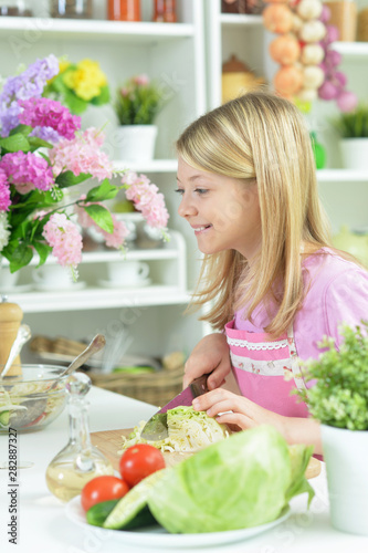 Cute girl preparing fresh salad on kitchen table at home