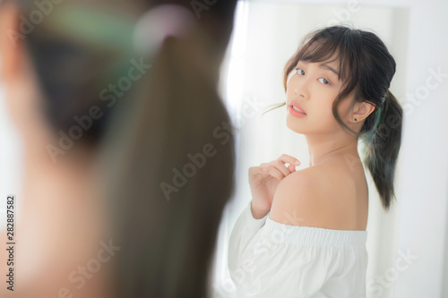 Beautiful asian woman with clothes trying on dressed up fitting with modern and looking reflect mirror in the room, girl choose clothes fashion with happy and cheerful, lifestyle concept.