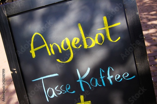 Close up of black chalk board with yellow and blue handwritten message (German text meaning: Offer cup of coffee) photo