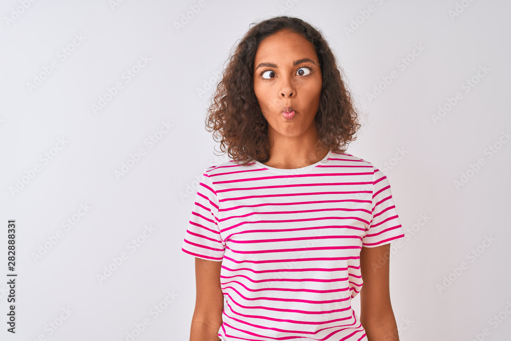 Young brazilian woman wearing pink striped t-shirt standing over isolated white background making fish face with lips, crazy and comical gesture. Funny expression. Young brazilian woman wearing pink striped t-shirt standing over isolated white background making fish face with lips, crazy and comical gesture. Funny expression.