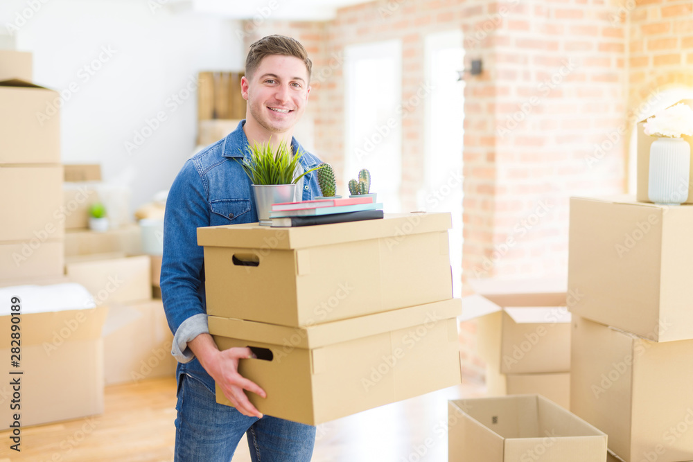 Handsome young man smiling happy moving to a new home, very excited holding cardboard boxes at new apartment Handsome young man smiling happy moving to a new home, very excited holding cardboard boxes at new apartment