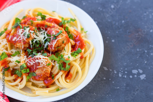 Spaghetti with meatballs, tomato sauce and parmesan cheese in white plate on dark background.