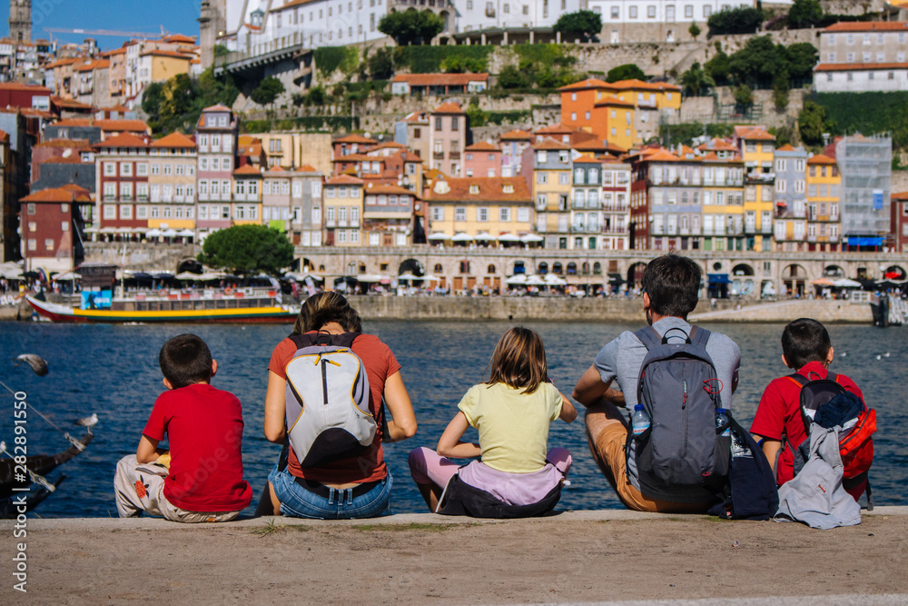 Porto, Portugal - 10/22/2019: Family back view sitting on embankment of river Douro, Porto, Portugal. Tourists in Portugal. Backpackers on aerial view of Porto. Portuguese vacation. Summer travel. 