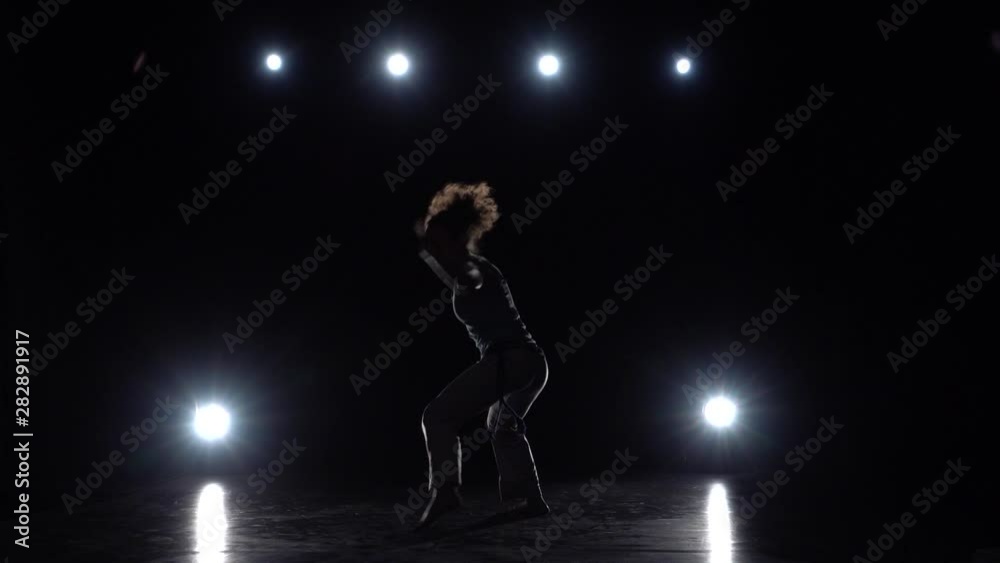 Brunette woman practicing capoeira in darkness against spotlight in studio. Brunette woman practicing capoeira in darkness against spotlight in studio.